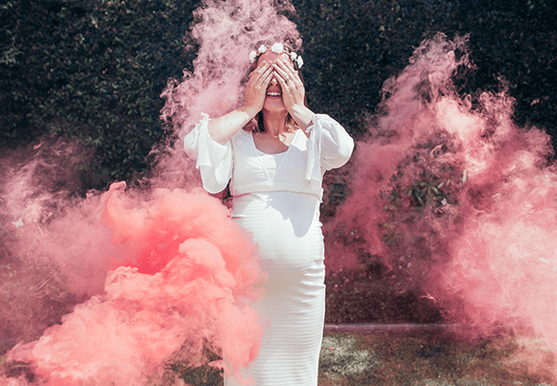 A happy woman covers her face smiling against a background of coloured smoke